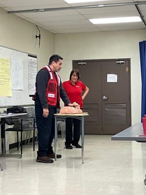 A man in a red vest demonstrating with a CPR mannequin